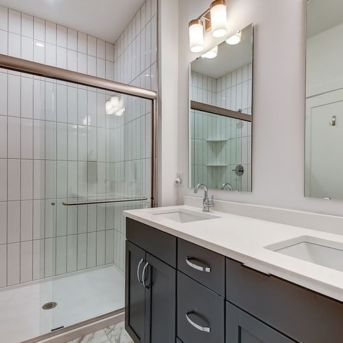 This modern bathroom features a sleek glass-enclosed shower with subway tiles, a double-sink vanity with white countertops, and stylish fixtures for a clean, contemporary look.