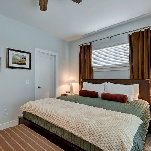 Primary bedroom with king bed featuring warm bedding, matching bedside tables, soft lighting, and natural light through large windows.