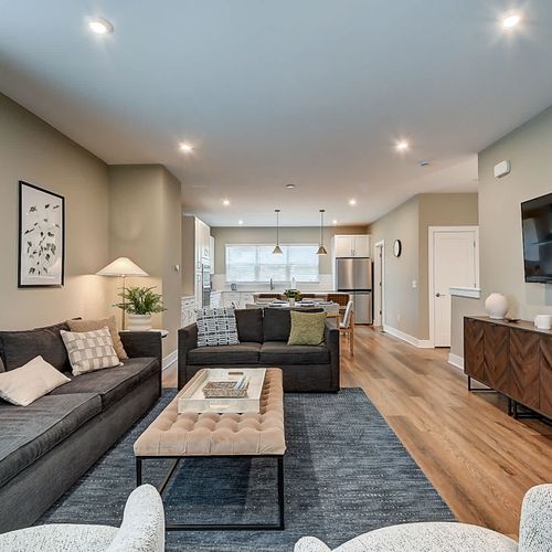 Step into your modern space, featuring a large couch, comfy chairs, and loveseat, TV, warm decor, and an open floor plan that seamlessly connects the dining and kitchen areas.