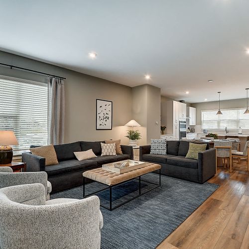 Step into your modern space, featuring a large couch, comfy chairs, and loveseat, TV, warm decor, and an open floor plan that seamlessly connects the dining and kitchen areas.