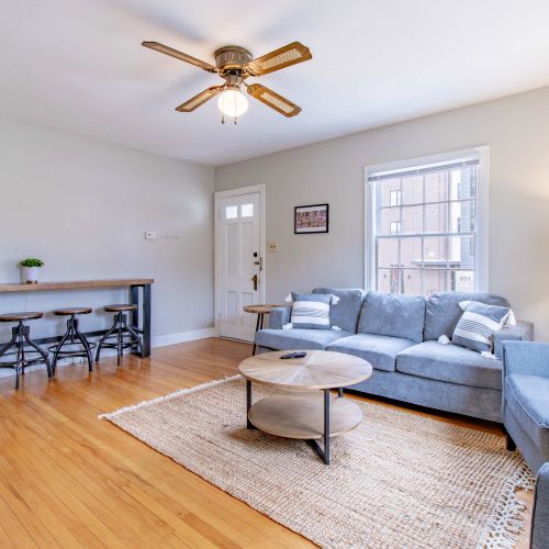 A cozy living room featuring a plush couch with soft throw pillows, two stylish accent chairs arranged for conversation, a sleek coffee table at the center, accompanied with a bar table and bar stools.