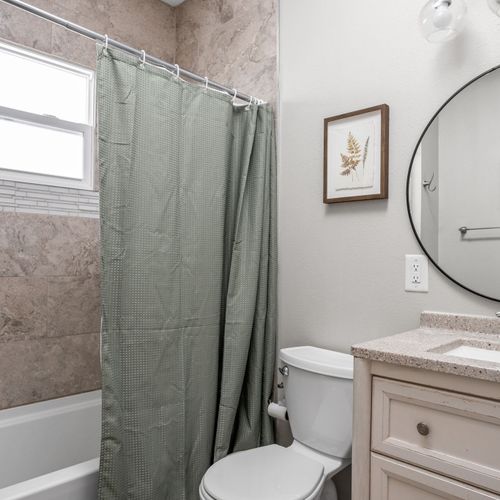 Relax in luxury in this full bath with a shower/tub combo, thoughtful decor, a modern vanity and mirror.