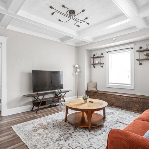 Step into our modern living room with industrial shelving and lighting. Featuring a comfy couch, thoughtful decor, and a smart TV for your convenience.