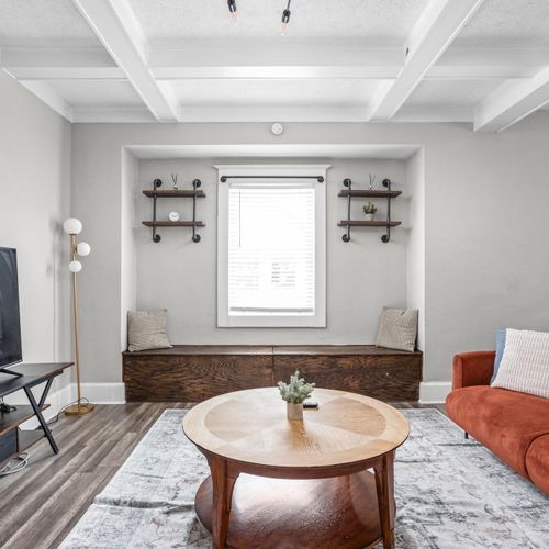 Step into our modern living room with industrial shelving and lighting. Featuring a comfy couch, thoughtful decor, and a smart TV for your convenience.