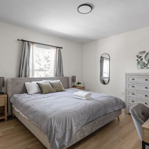 Step into the main bedroom! Featuring a king bed, modern decor, a dresser, and a desk.