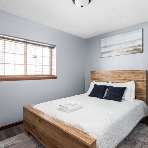 This queen bedroom features natural light, cozy decor, and a nightstand.