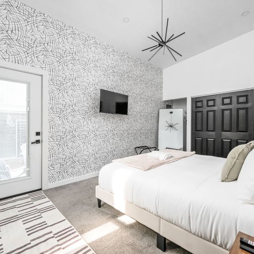 Chic black & white wallpaper, king-size luxurious bed, smart TV, and iconic Indy art—master bedroom done right.