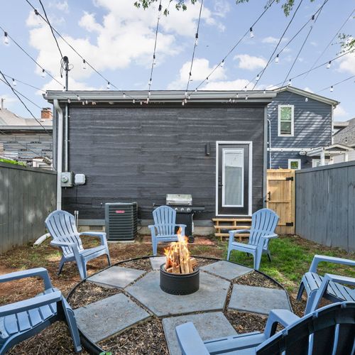 Kick back in the backyard by the modern stainless steel fire pit, blue chairs, games, and grill—outdoor vibes done right.