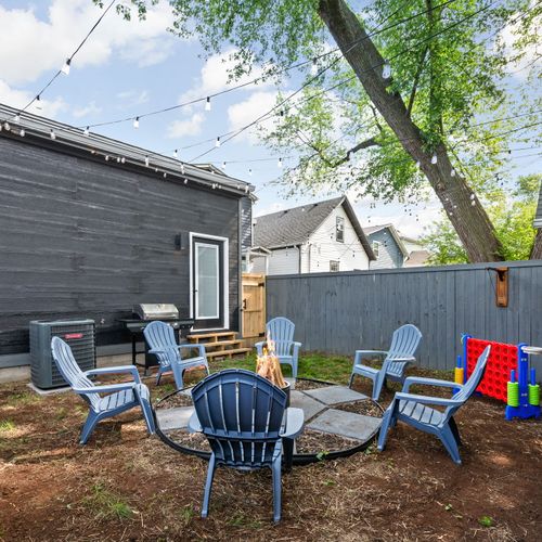 Kick back in the backyard by the modern stainless steel fire pit, blue chairs, games, and grill—outdoor vibes done right.
