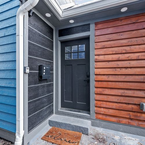 Welcome home — dark wood door with wood paneling, bold black and blue siding for serious curb appeal.