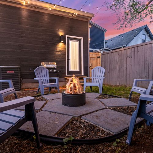 Kick back in the backyard by the modern stainless steel fire pit, blue chairs, games, and grill—outdoor vibes done right.