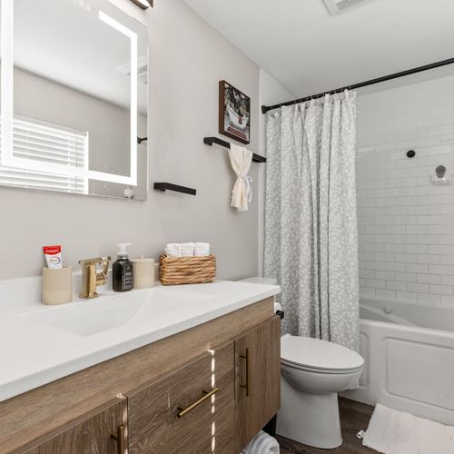 Fresh, bright bathroom with a lighted mirror, clean finishes, and a tub-shower combo for easy resets.