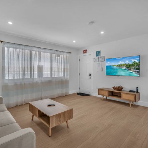 Simple yet cozy living area featuring a comfy sofa, airy natural light, and a dining space, perfect for relaxing after a day at the beach or a calm night in.