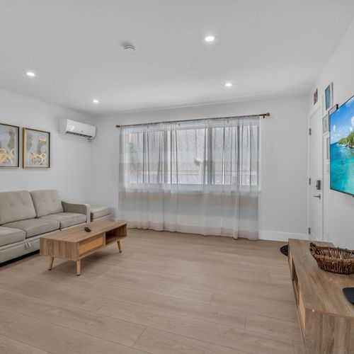 Simple yet cozy living area featuring a comfy sofa, airy natural light, and a dining space, perfect for relaxing after a day at the beach or a calm night in.