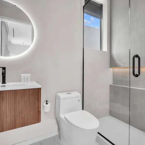 Step into a bright, refreshing oasis. This guest bathroom offers a luxurious, spa-like feel with its modern walk-in glass shower, premium rain showerhead, and a stylish wood-paneled vanity.