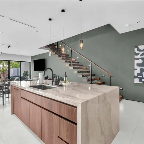 This high-end culinary space features a stunning contrast between warm wood lower cabinets and minimalist white floor-to-ceiling storage, anchored by a massive marble-style waterfall island.