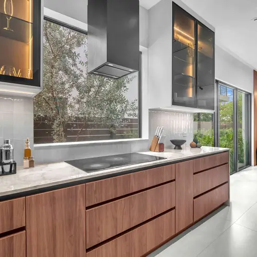 This high-end culinary space features a stunning contrast between warm wood lower cabinets and minimalist white floor-to-ceiling storage, anchored by a massive marble-style waterfall island.