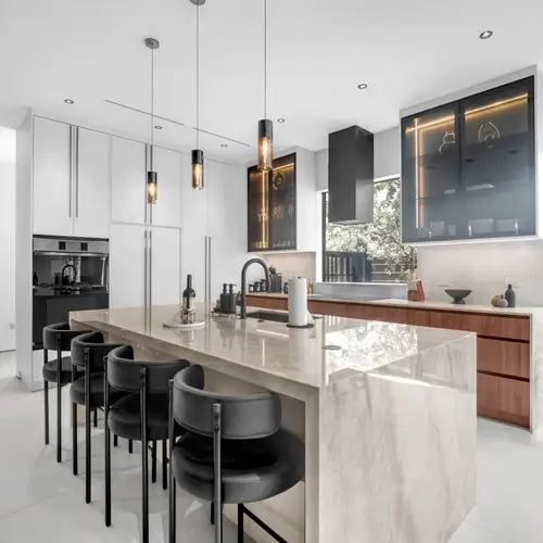 The layout highlights a functional yet stylish design with black leather bar stools, professional-grade matte black fixtures, and glass-front upper cabinets with integrated LED accent lighting.