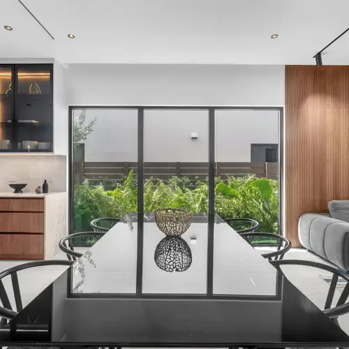 Perfectly set for entertaining, this room showcases a sleek dark wood dining set, premium glassware, and a warm, inviting atmosphere created by the architectural wood accents and minimalist design.