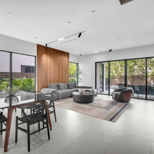 The room highlights an elegant neutral color palette, premium area rugs, and floor-to-ceiling windows that fill the modern interior with abundant natural light.