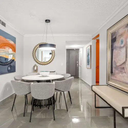 Entry hallway with upholstered bench and large framed artwork, leading to the round dining table with sunburst mirror and the front door.