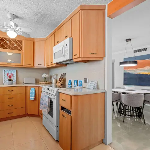Kitchen with wood cabinets, white range and microwave, opening onto the dining area with round table and abstract artwork.