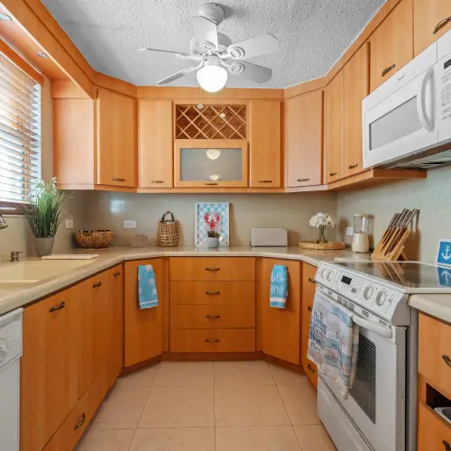 U-shaped kitchen with wood cabinetry, built-in wine rack, white electric range, over-range microwave, dishwasher, double sink and ceiling fan.