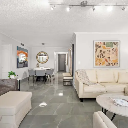 Living room with gray sofa and ottoman, cream sectional and oval marble coffee table, looking toward the round dining table and entry hall.