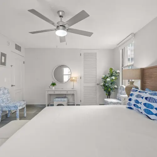 King bedroom toward the vanity table with round mirror, blue toile chair, louvered closet and doors to the ensuite bath.