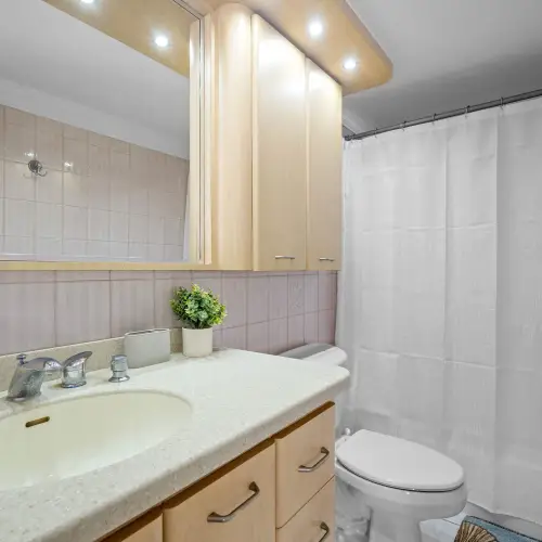 Bathroom with speckled countertop, wood vanity, wide mirror, recessed lighting, toilet and tub with white shower curtain.