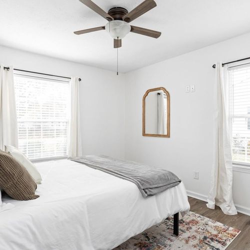 A welcoming bedroom adorned with an elegantly appointed queen bed and two windows, establishing a bright and inviting atmosphere.