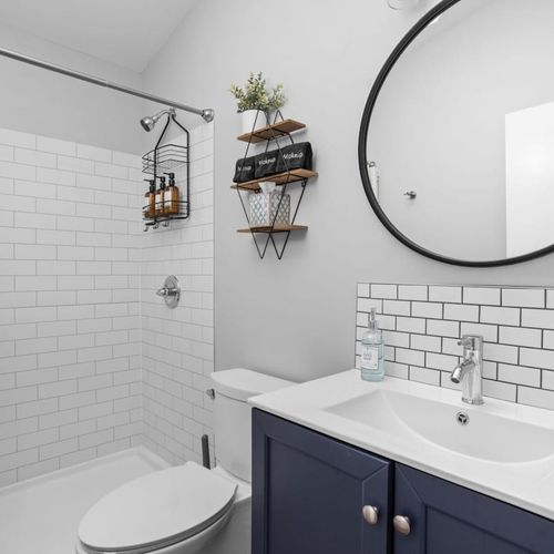 Step into our strikingly elegant full bathroom, featuring a clean mirror, sink, fresh towels, and essential toiletries, creating a refined and well-appointed space.