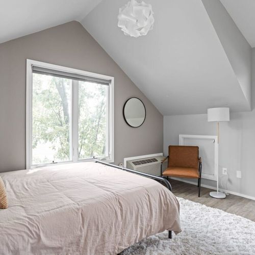 Experience comfort in our bedroom with a queen bed adorned with clean, soft pillows and linens. Accompanied by a bedside table, additional seating, and a working table, creating a well-appointed and functional space.