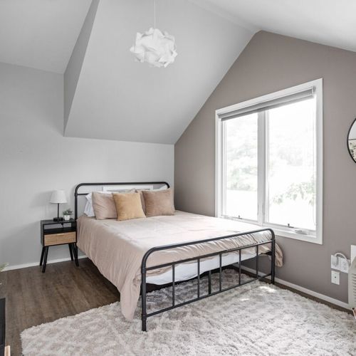 Experience comfort in our bedroom with a queen bed adorned with clean, soft pillows and linens. Accompanied by a bedside table, additional seating, and a working table, creating a well-appointed and functional space.
