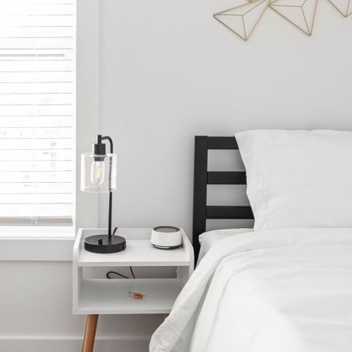 Enhance your bedroom experience with a bedside table, a soothing bedside lamp, and a white noise machine for added comfort and relaxation.