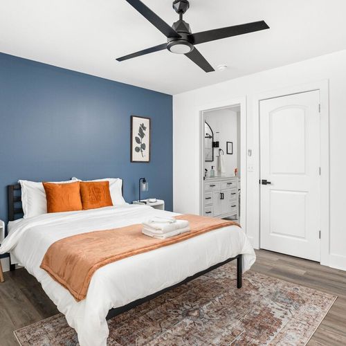 Experience the comfort of a queen-sized cozy bed complemented by a mirror, bedside table with a lamp, framed wall decor, an attached bathroom, for your stay.