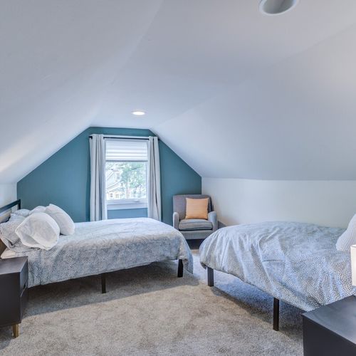 Enjoy our bedroom featuring one cozy double bed and one single bed, adorned with fresh towels, soft pillows, and freshly laundered linens. Complete with a bedside table, lamp, and additional seating near the window, it's a perfect retreat for your comfort.