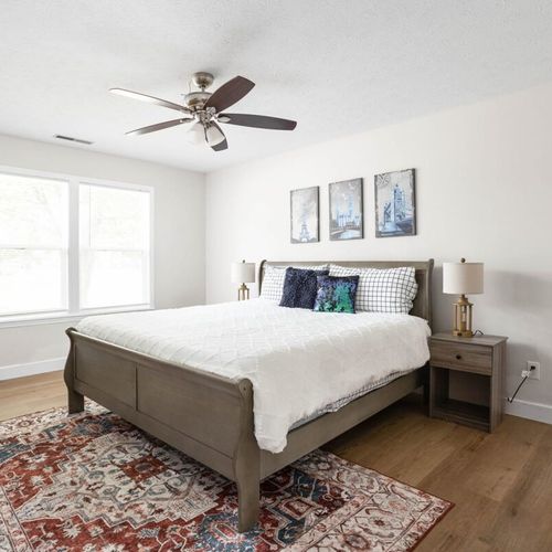 Welcome to the inviting bedroom with a queen-size bed, comfy pillows, bedside table with a lamp, framed walls, and a cozy window seat. Enjoy your stay!