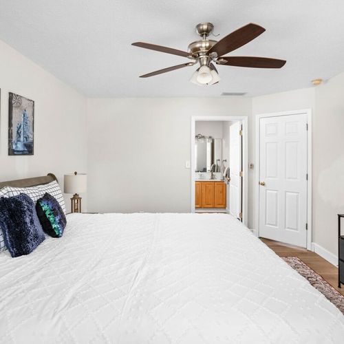 This welcoming bedroom features a queen-size bed, plush pillows, bedside table with a lamp, framed walls, cozy window seating, dresser, and TV.