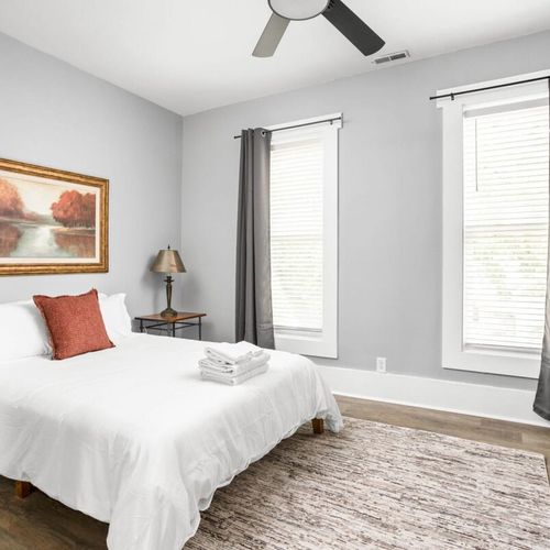 The bedroom's charm with a great window allowing natural light, complemented by a bedside table and lamp, a dresser for storage, and the added comfort of a futon.