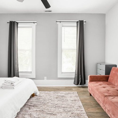 The bedroom's charm with a great window allowing natural light, complemented by a bedside table and lamp, a dresser for storage, and the added comfort of a futon.