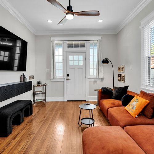 Kick back on the plush orange sectional in this bright living room w/ warm wood floors & a light-filled front entry