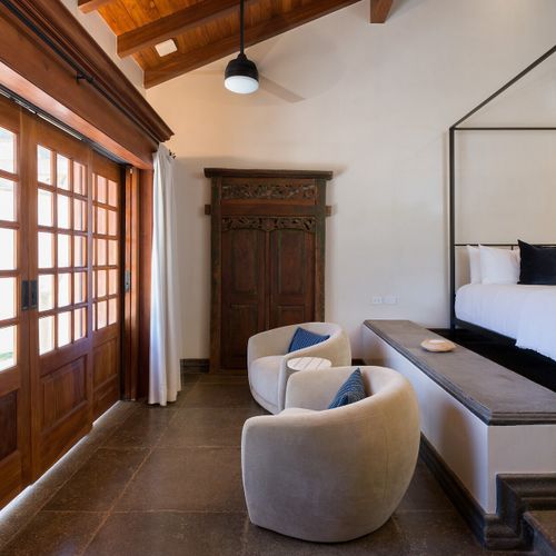 Four-poster king suite - hand-carved antique doors, curved velvet armchairs, exposed-beam wood ceiling.