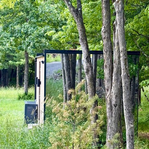 Nestled among the trees, the mirrored retreat reflects the summer woods on every side.