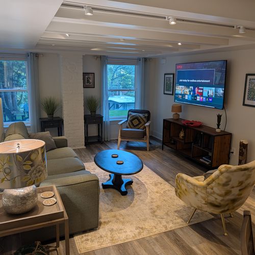LIVING ROOM (FIRST FLOOR):  The home has a beautiful living room with a sofa, chairs, coffee table, lamps, and a large screen television.