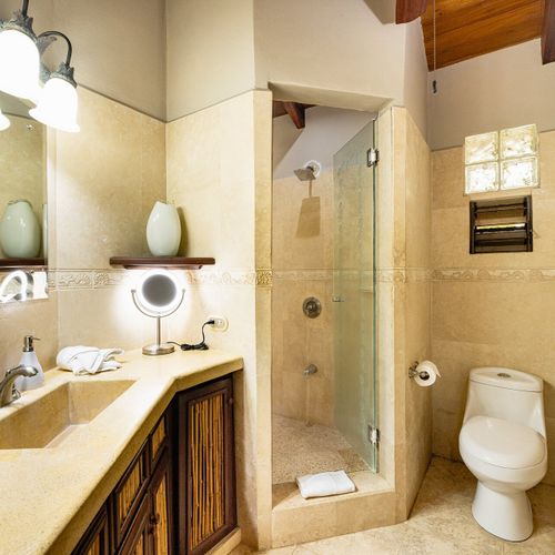 ravertine ensuite bath with glass shower stall, glass-block window and brass sconces at Casa Blue Lagoon, Tamarindo, Costa Rica.