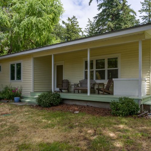 Peaceful cottage surrounded by trees, featuring a covered front porch with comfortable seating to relax and enjoy the fresh island air.