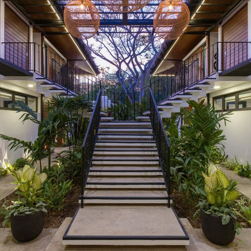 Lit courtyard staircase between Casa Oso villa wings at twilight with tropical foliage and pendant lights, Tamarindo, Costa Rica.