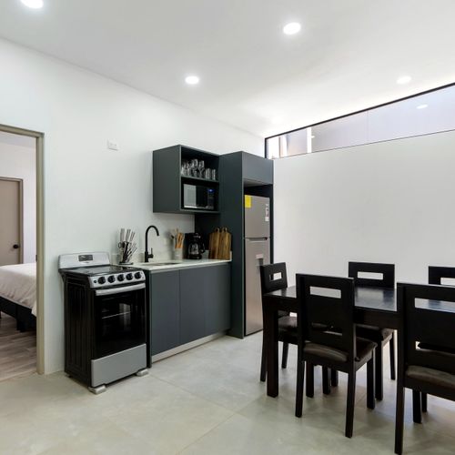 Galley-style kitchen with stainless refrigerator, four-burner range, and dining table for five, adjacent to bedroom access in Casa Margarita, Tamarindo.