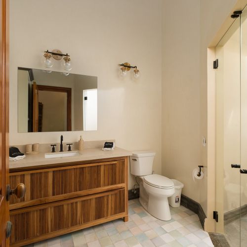 Ensuite bath - fluted teak vanity, brass globe sconces, walk-in shower, soft pastel floor.